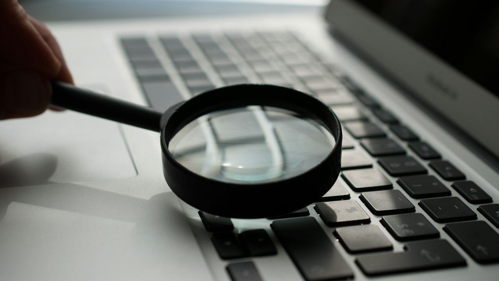 A magnifying glass near a laptop, representing independent AI safety evaluation in the Anthropic Accenture partnership
